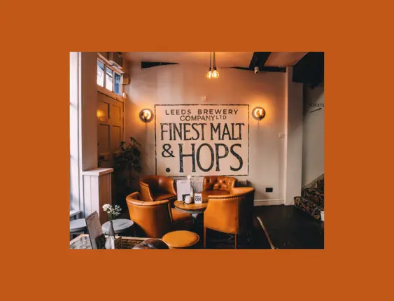 Warm pub interior with leather armchairs, under a sign reading 'Leeds Brewery Company Ltd Finest Malt &amp; Hops'.