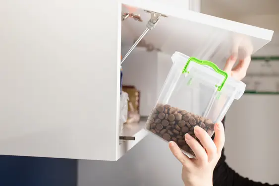 Someone puts away kibble in a cupboard, the kibble is stores in a plastic box